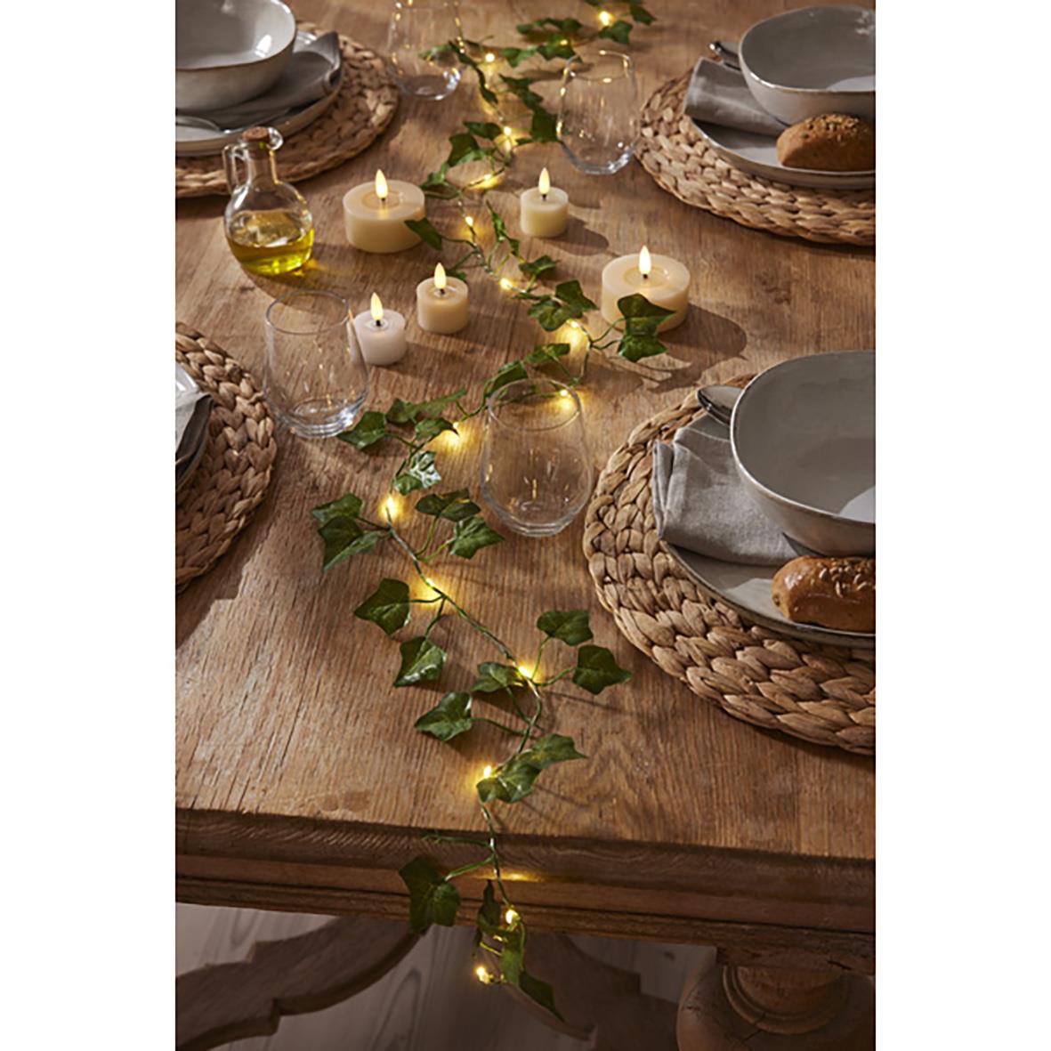 Ljusslinga Ivy med gröna blad och små ljus på ett träbord med dukade tallrikar och glas