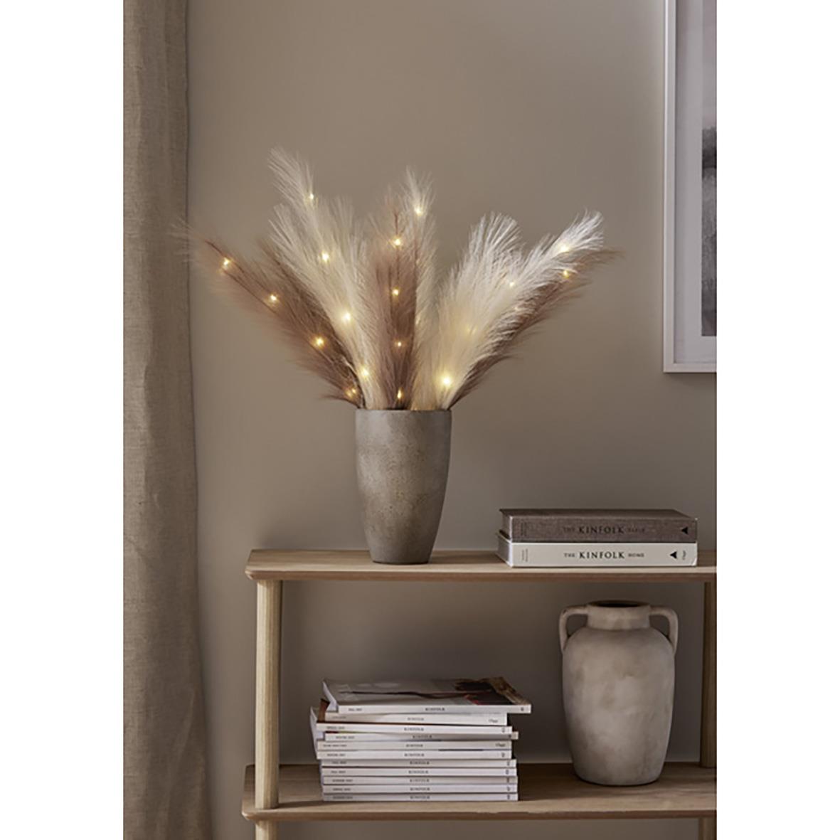 Dekorationskvist med bruna och vita fjädrar med små ljus, i en grå kruka på ett träbord