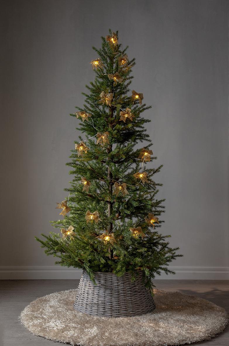Liten julgran med ljusslinga och guldstjärnor, placerad i en väsad korg på en matta
