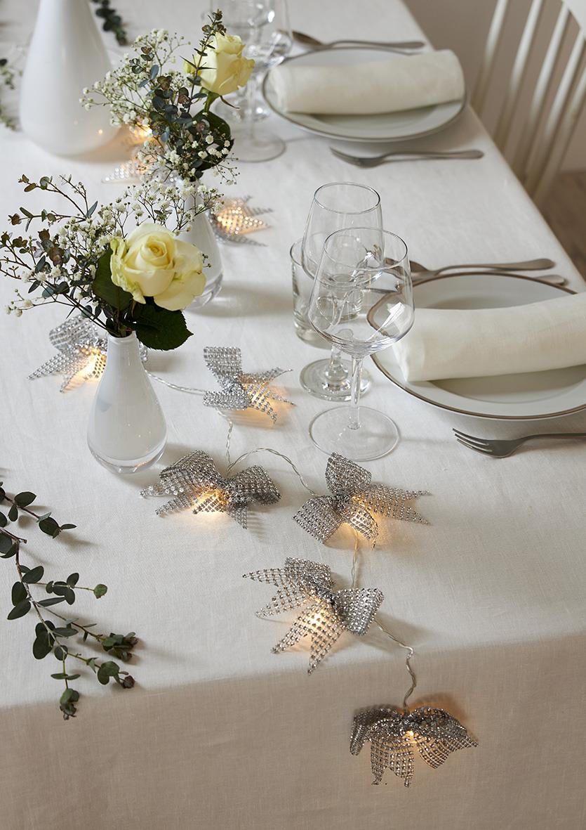 Vitt borddukning med blomsterarrangemang och ljusslinga Star Trading Bowie Silver på bordet