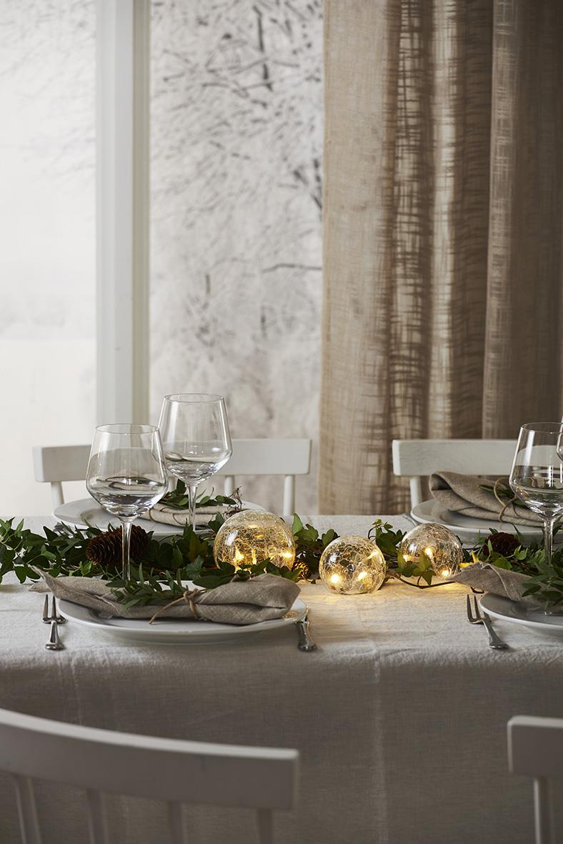 Dekorerat bord med glasdekoration Star Trading Triss Klar, ljuslyktor och gröna blad i ett hem med fönster och gardiner