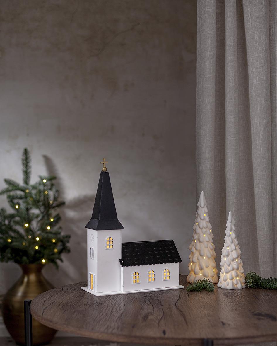 Vit juldekoration med kyrka och snötäckta granar på ett runt bord, vintertema inomhus