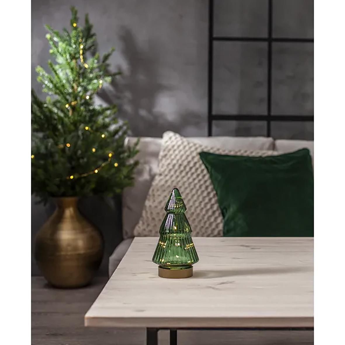 Grön glasdekoration i form av en julgran på ett bord med julgran i bakgrunden