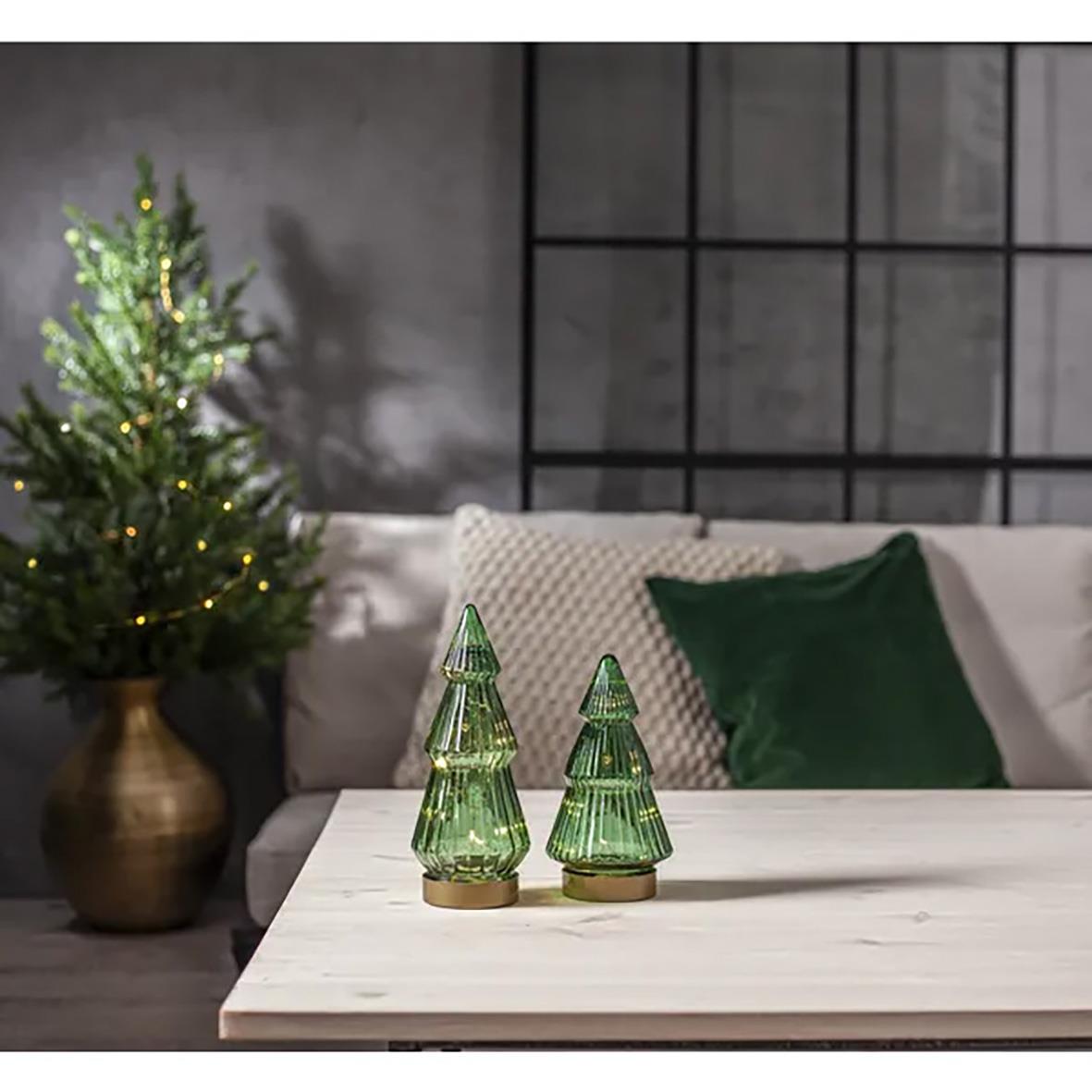 Gröna glaskonstnärliga julgransdekorationer på ett bord med ett julgran i bakgrunden