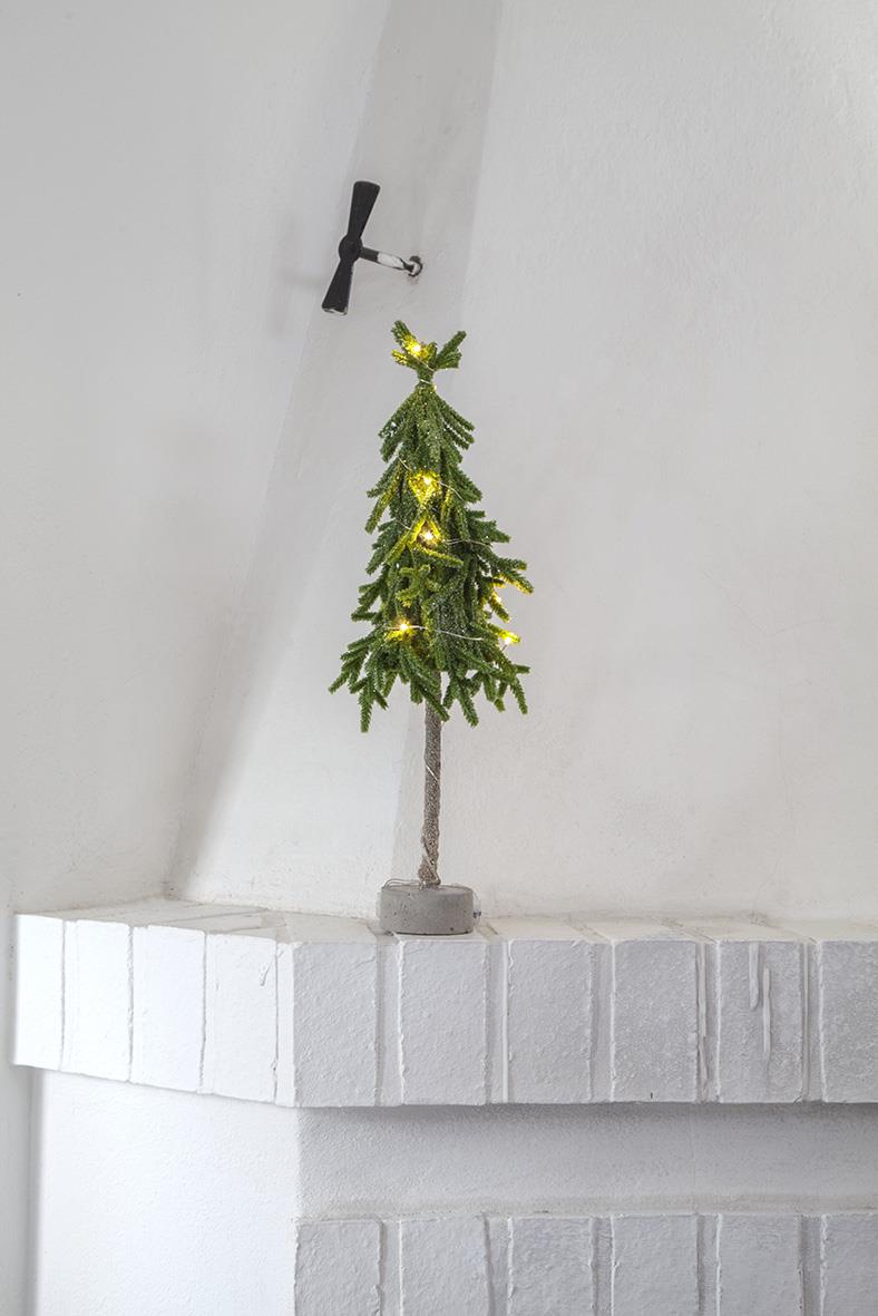 Grön juldekoration av en liten trädliknande form med ljus, 45 cm hög, placerad på en vit mur