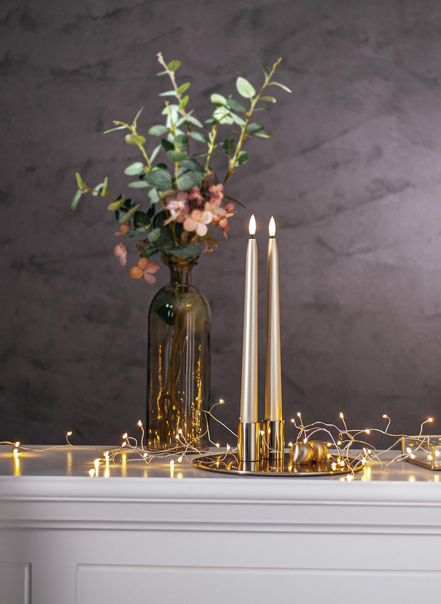 Antikljus Star Trading LED Flamme i guldfärgad metall på vit yta med blommor och ljusslinga