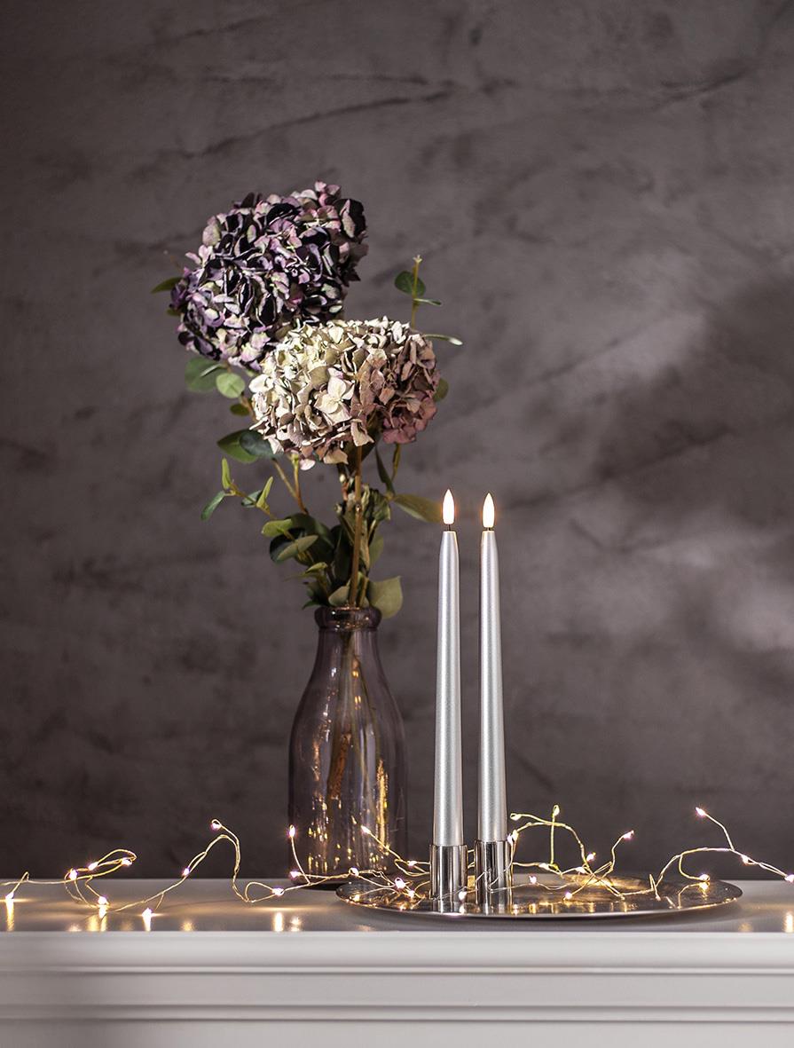 Vas med blommor, LED-ljus i silverfärgad lykta, och julbelysning på bord mot grå bakgrund