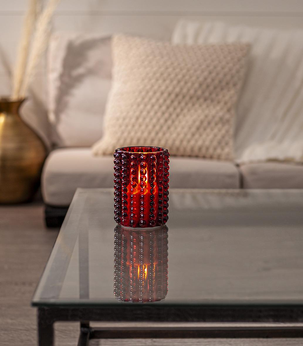 Röd glaslykta med LED-flamma på ett soffbord i ett vardagsrum
