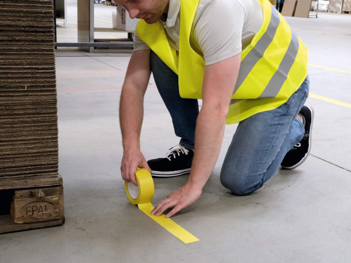 Person som sätter upp gul golvtejp på betonggolv i lagerlokal