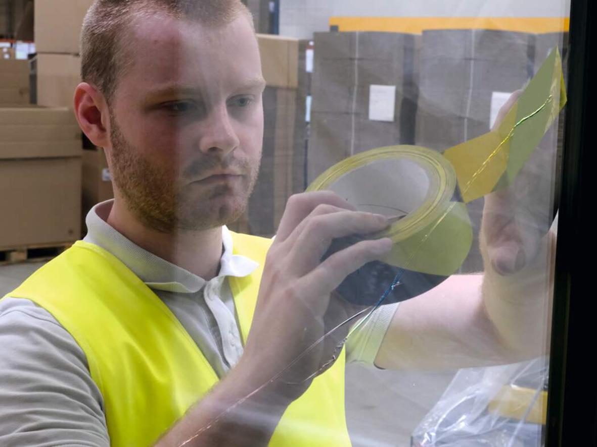 Man i gul väst sätter varningstejp på glasruta i lagerlokal