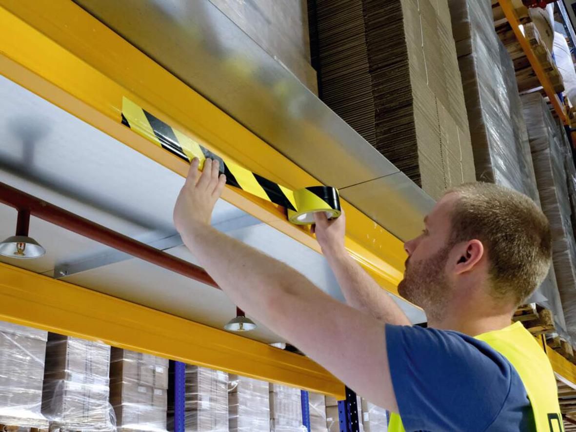 Man placerar varningstejp på lagerhylla i lagerlokal