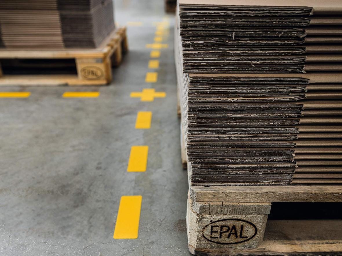 Golvmarkering med kort gul streck i lagerlokal bredvid staplade material