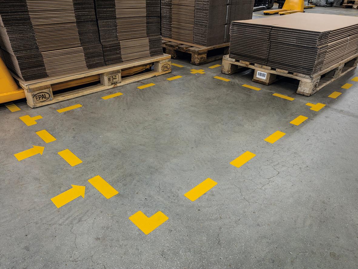 Guldfärgade golvmarkeringar i L-form på betonggolv i lager eller verkstad