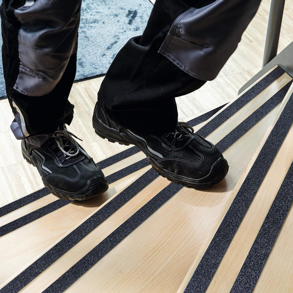 Person står på halkskyddstejp i svart med svarta skor, på en träbänk