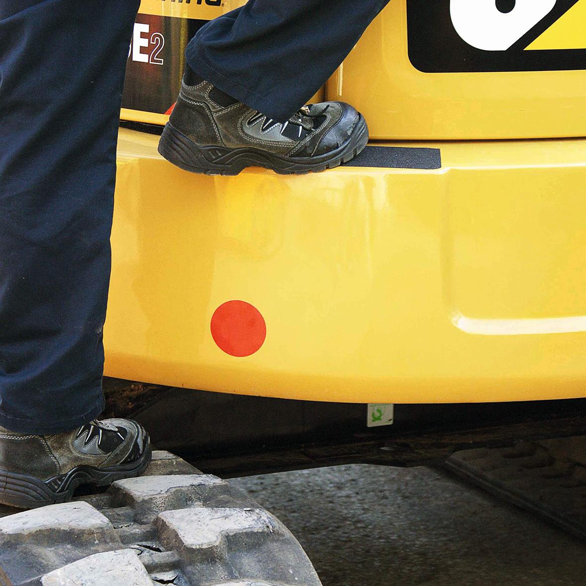 Person som går på halkskyddstejp på en gul maskin, svart sko och blå byxor