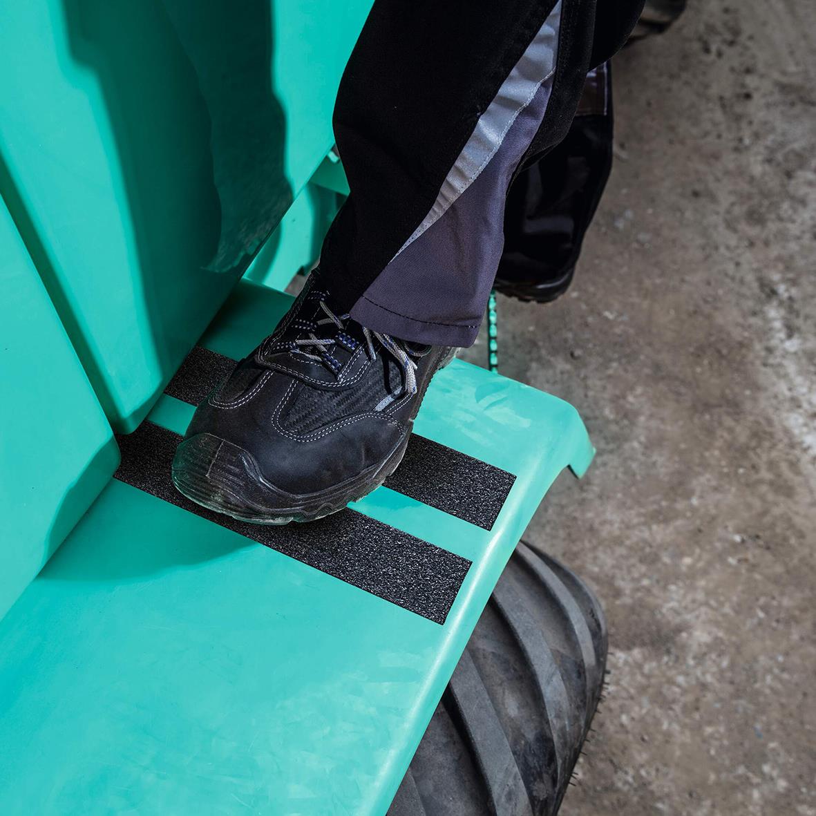 Person står på halkskyddstejp på en stol i ett verkstadsmiljö