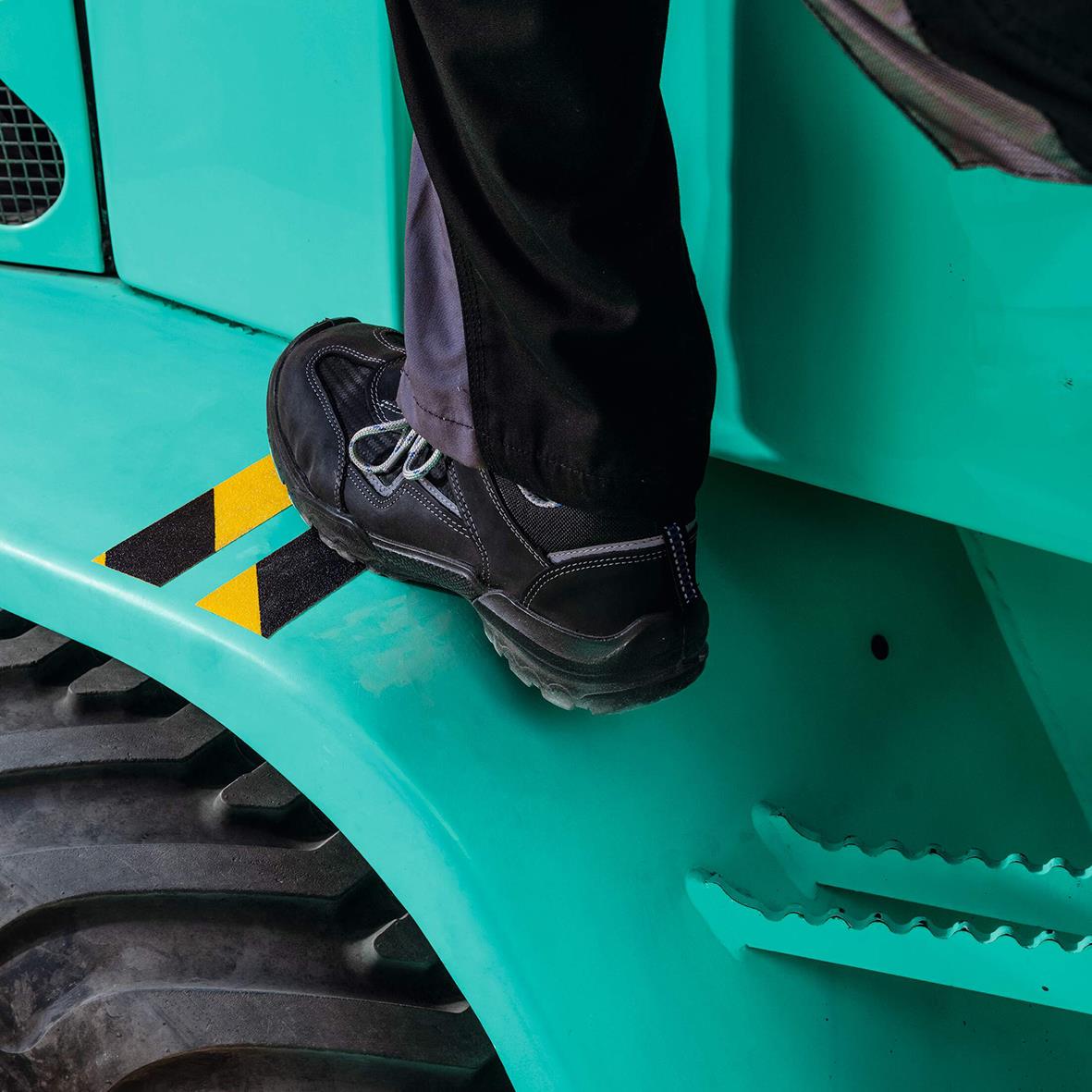 Person står på halkskyddstejp på en maskin eller fordon i gul/svart färg