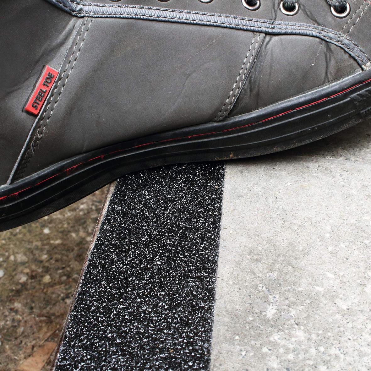 Halkskyddstejp på marken under en sko för att förhindra halka, svart med grått och svart skosula