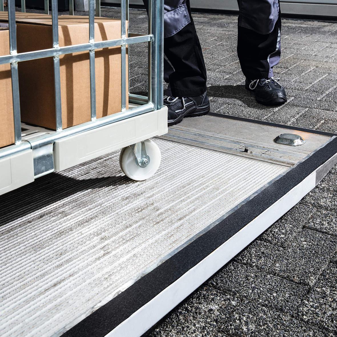 Halkskyddstejp på golv med en person i bakgrunden, svart och grått, för att förhindra halka