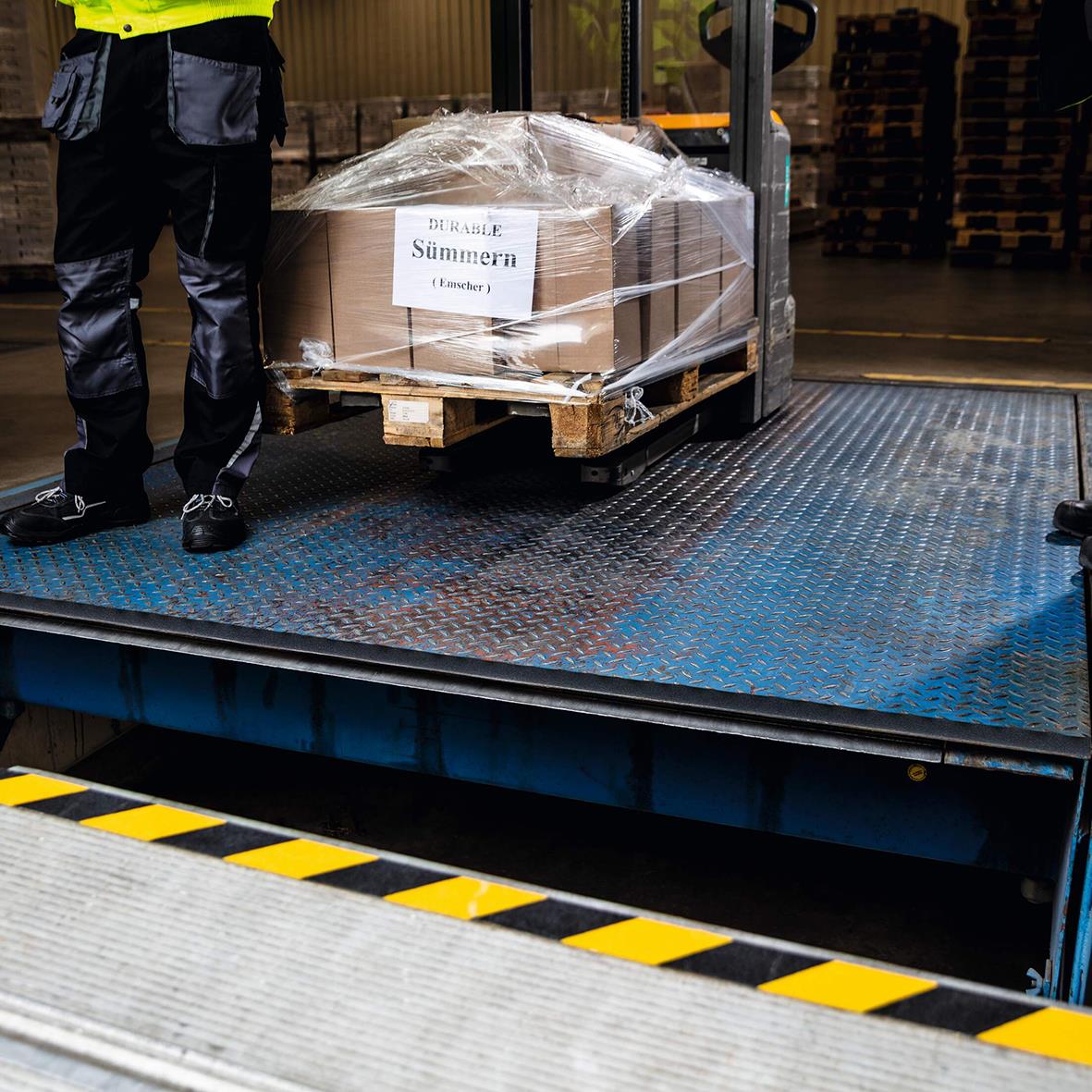 Person lastar en pall med stora kartonger på en lastbil med halkskyddstejp