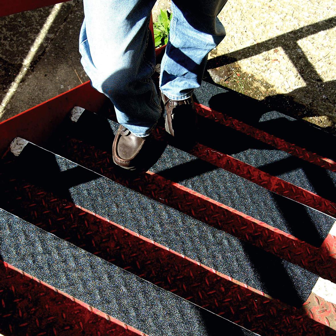 Person står på halkskyddstejp på trappa, svart med röd kant, för säkrare steg