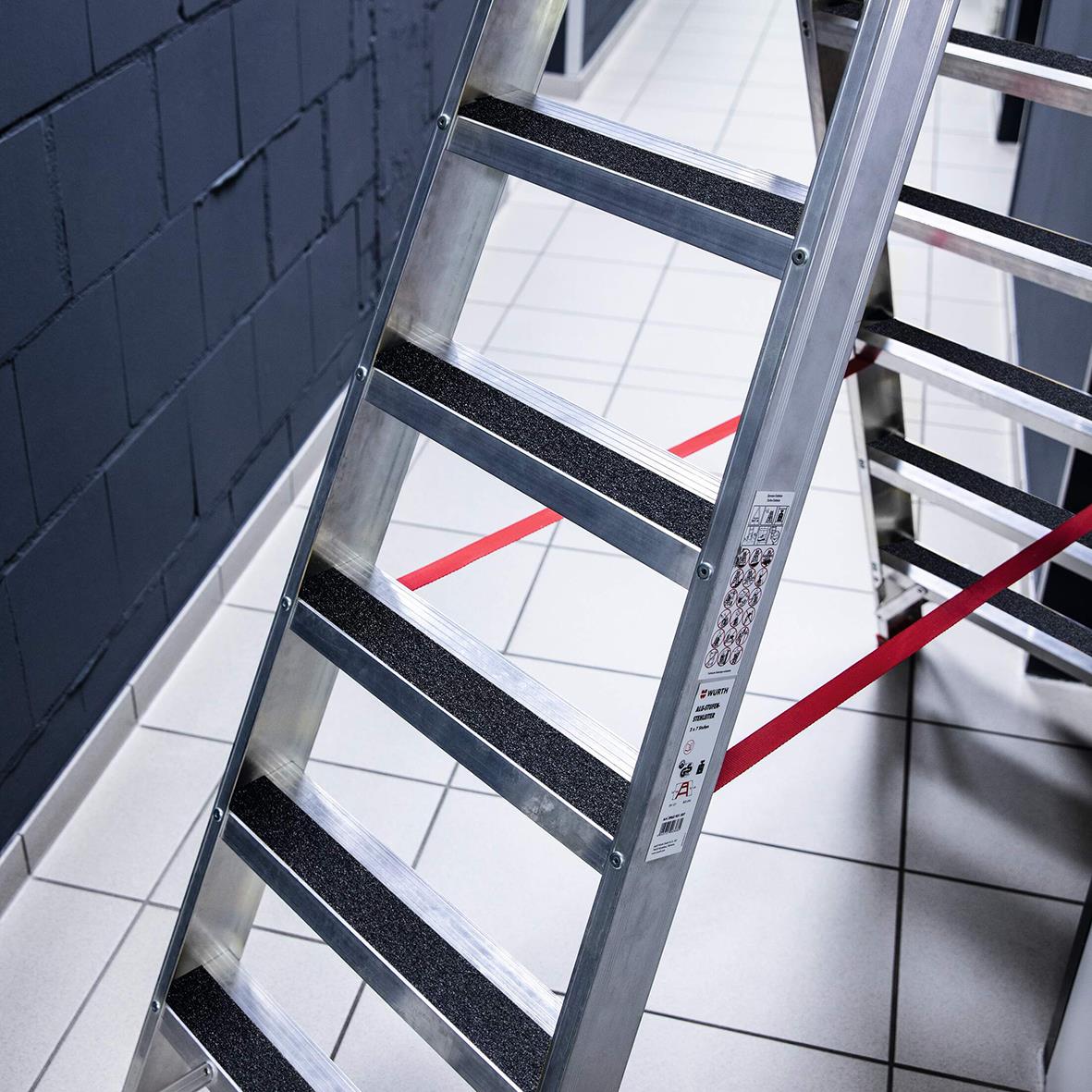 Laddstege med halkskyddstejp på stegen, svart och 50mm bred, placerad mot en vägg med mörk bakgrund