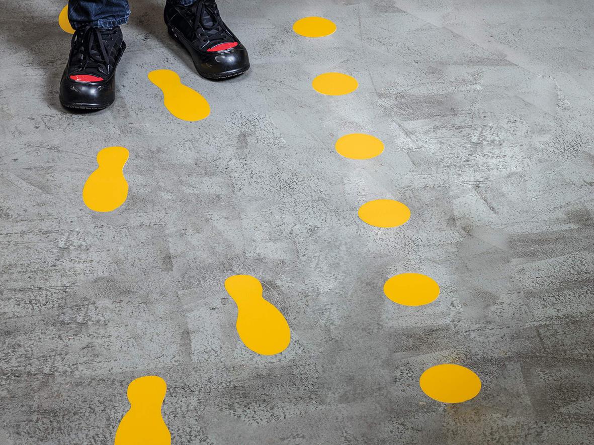 Gul självhäftande golvmarkering i form av prickar och fotavtryck på betonggolv