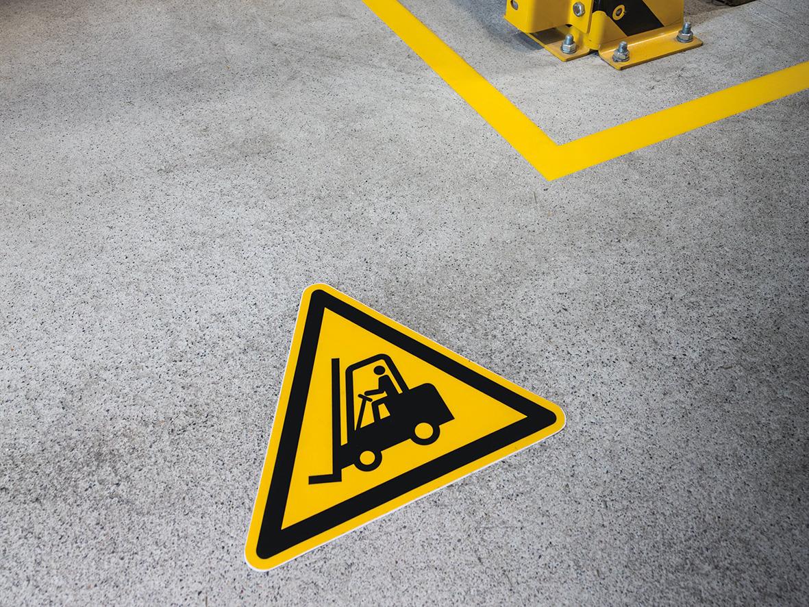 Varningsskylt för truckar, gul med svart symbol, placerad på betonggolv