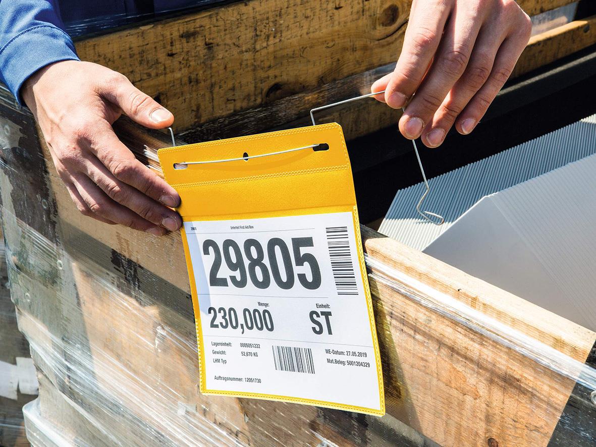 Person som fäster en gul plastficka med trådbygel på en träskiva