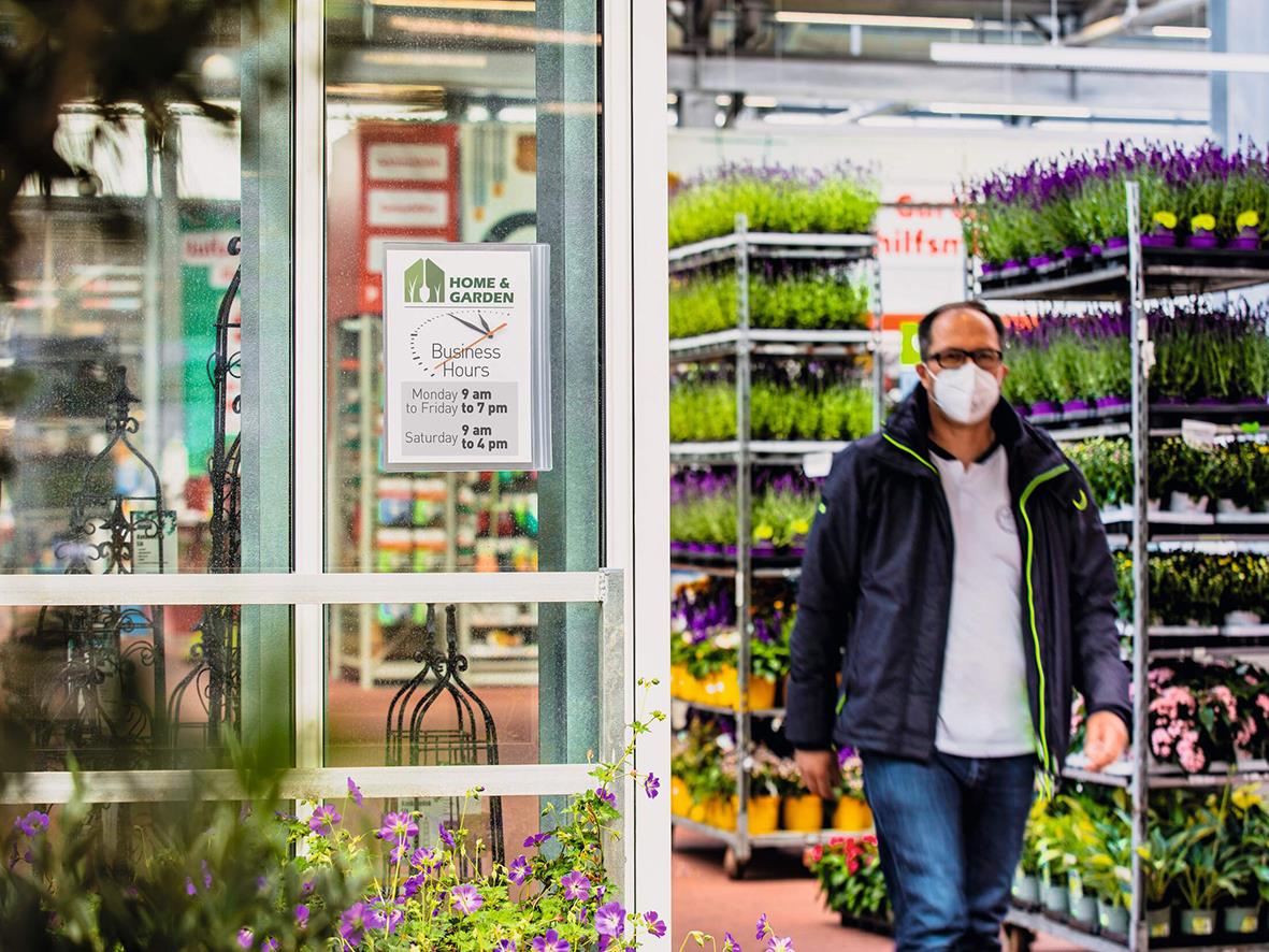Man med ansiktsmask som går ut från en växtbutik med hyllor av blommor och växter