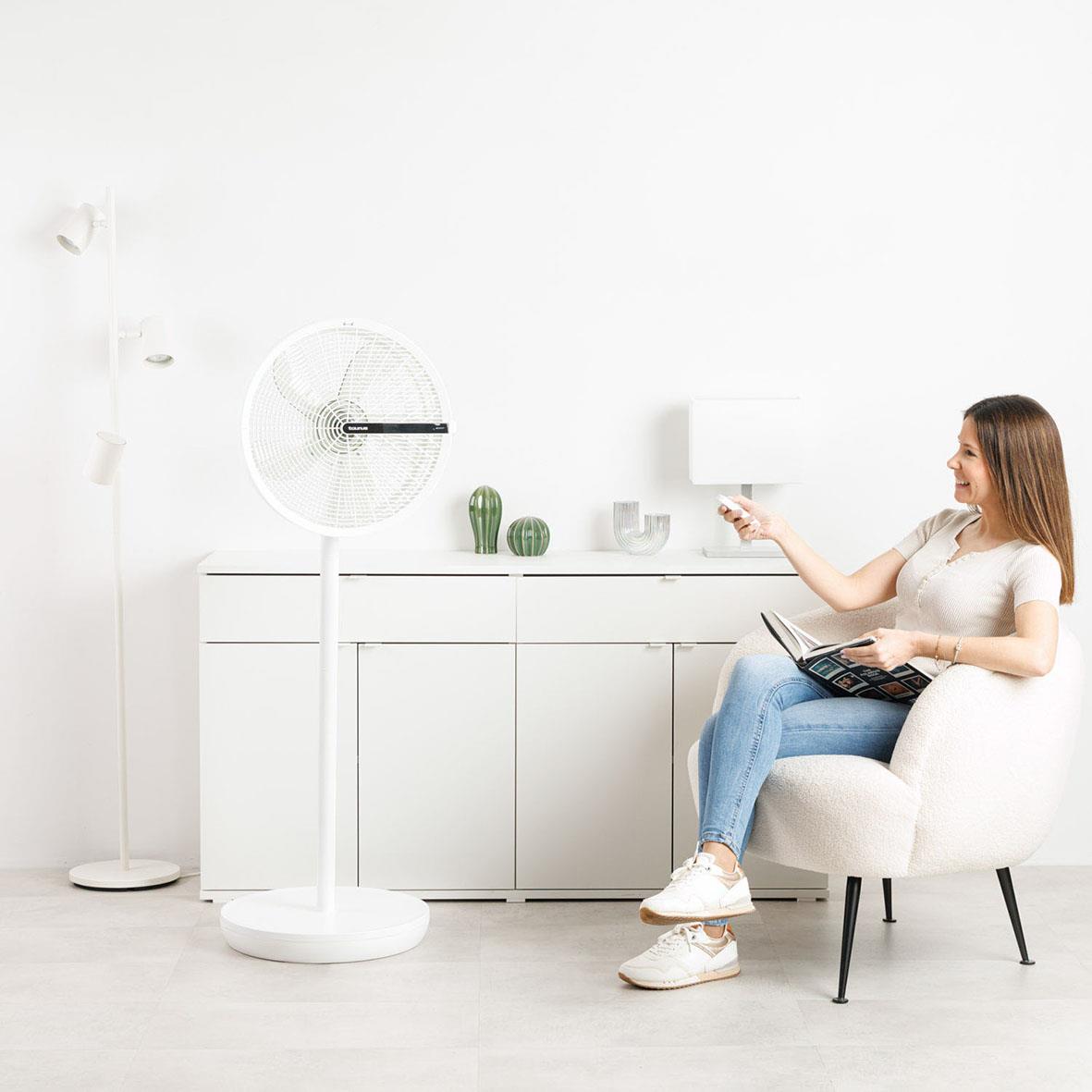 Kvinna sitter i en vit soffa i ett vitt rum med en golvfläkt Taurus Ice Brise 3-i-1