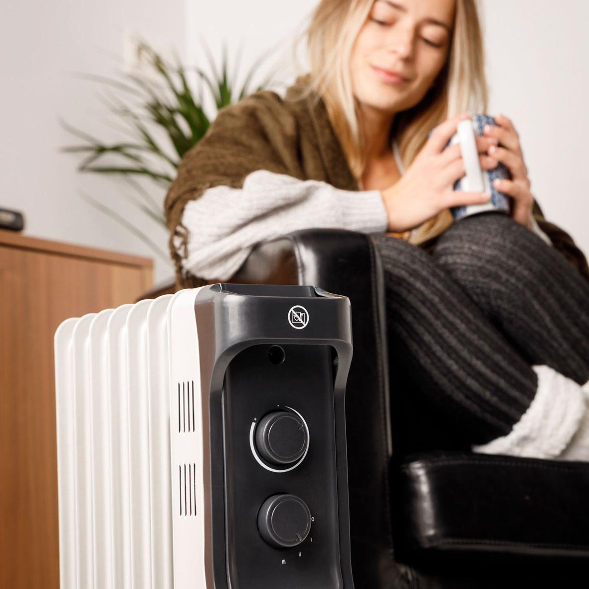 Kvinna som sitter på en soffa och håller en kopp, med Element Targus Oljeradiator New Dakar 1500 i förgrunden