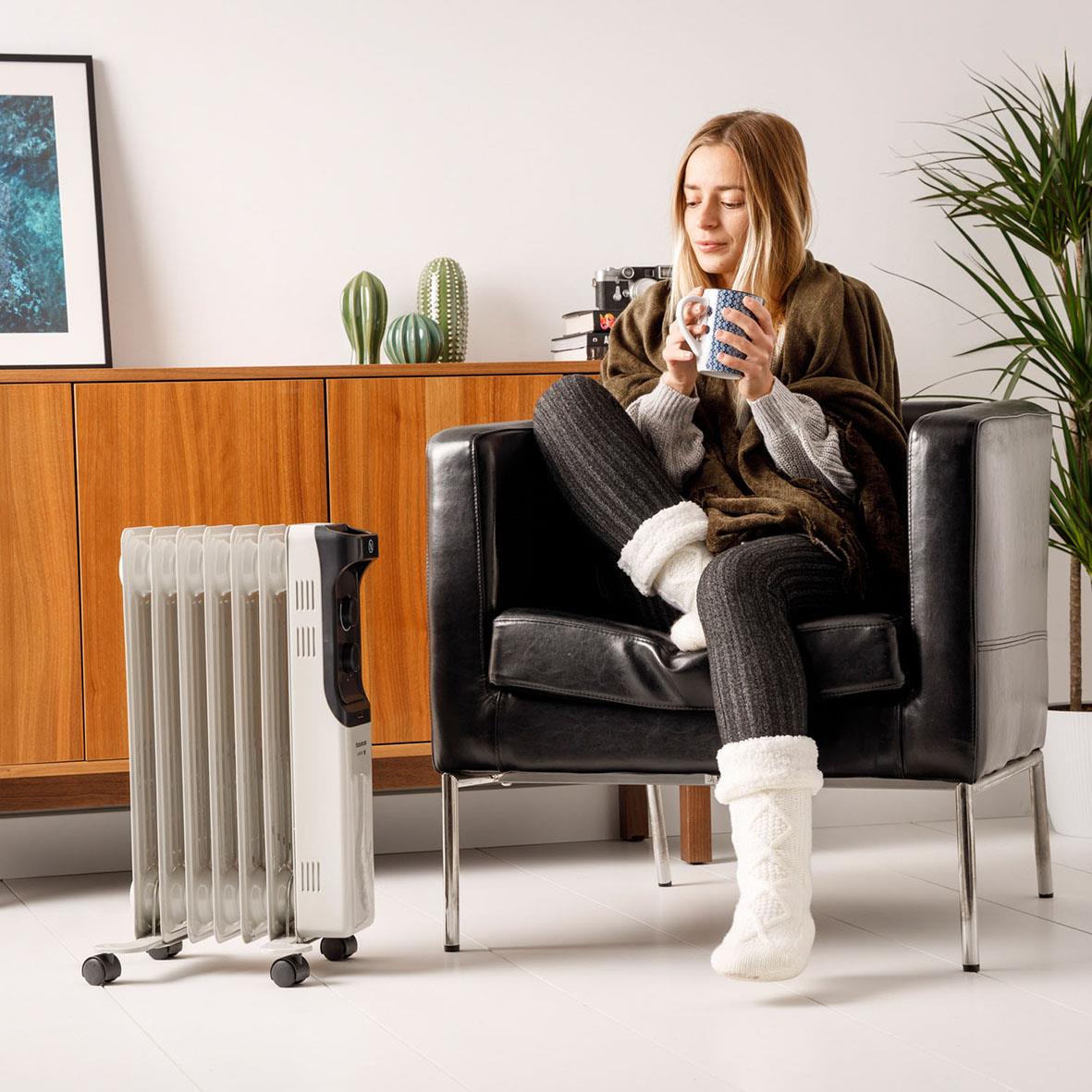 Kvinna sitter i en svart fåtölj med en Element Targus oljeradiator New Dakar 2000 bredvid sig, dricker ur en mugg