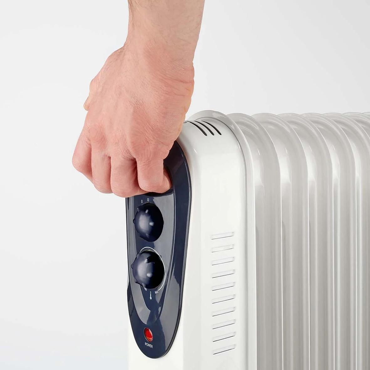 Hand som justerar en vit radiator med kontrollpanel och två rattar