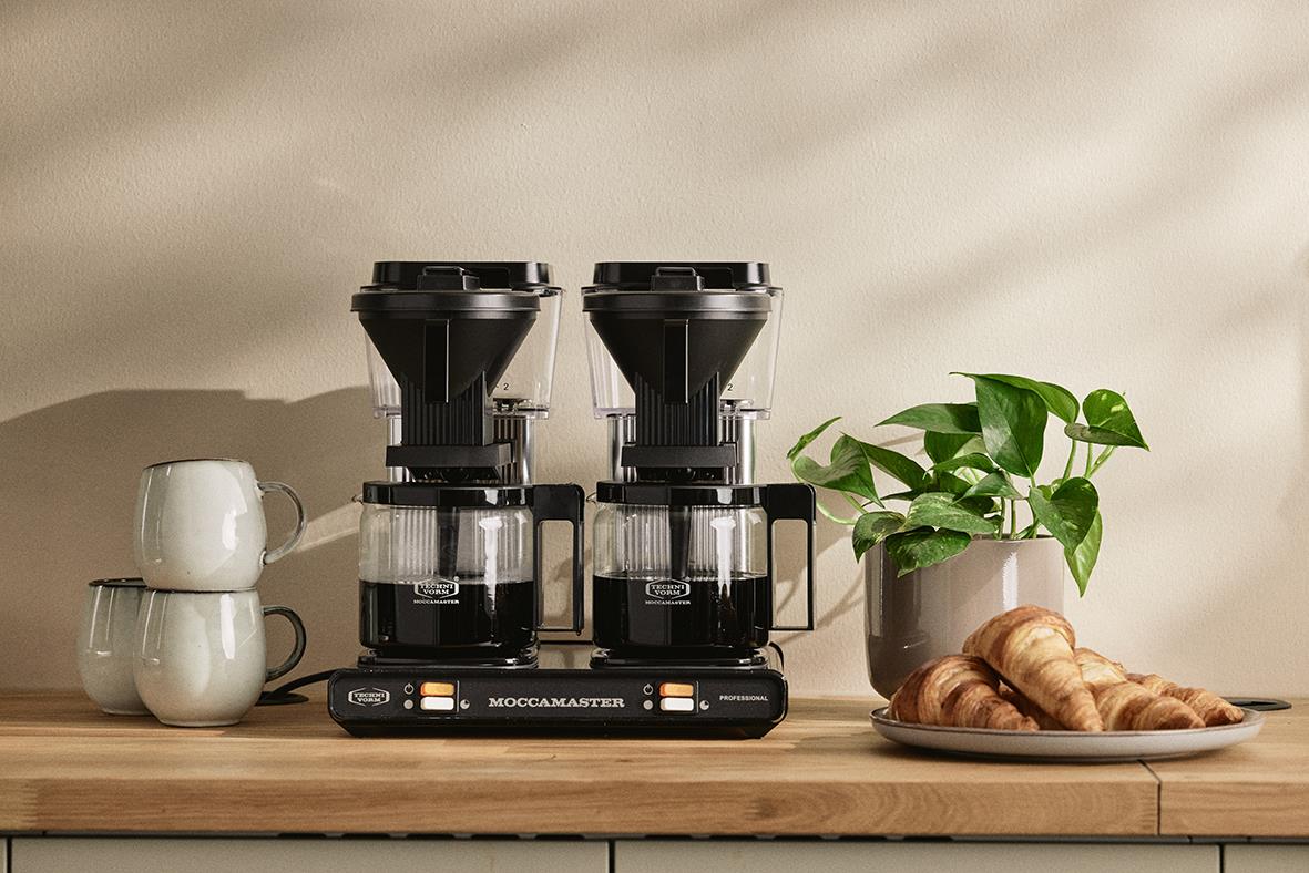 Kaffebryggare Moccamaster Professional dubbel svart/silver på köksbänk med koppar och växt