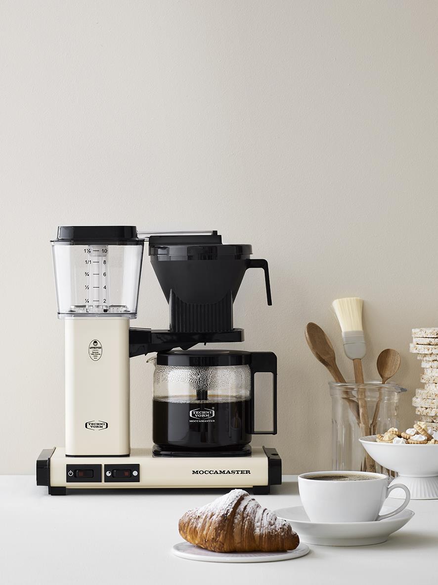 Kaffebryggare Moccamaster Automatic Light Ivory med kaffekopp, croissant och köksredskap på bordet