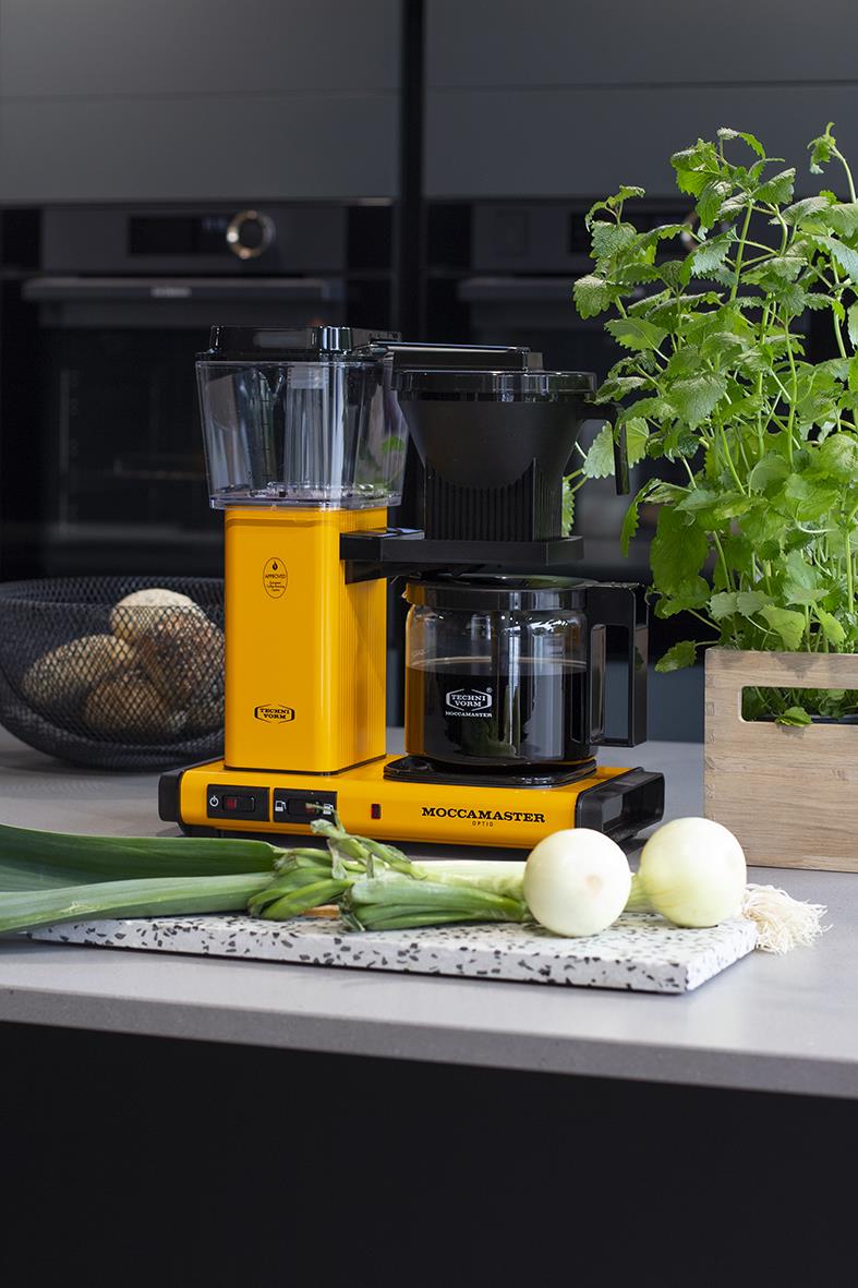 Kaffebryggare Moccamaster Optio Yellow Pepper på köksbänk med grönt växt och grönsaker