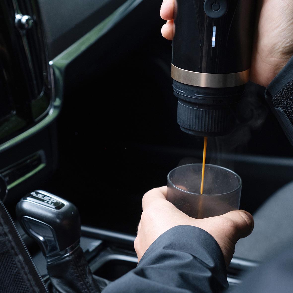 Person som använder en batteridriven espressomaskin för att hälla kaffe i ett glas i bilen