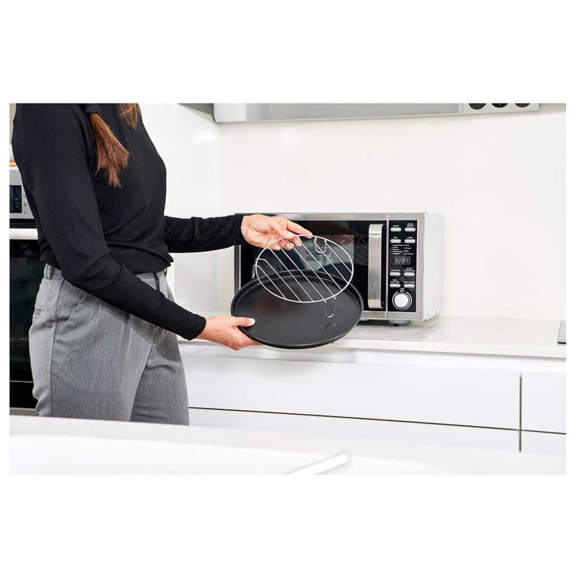 Person placerar ett rostfritt stålspett i en svart mikrovågsugn på köksbänk
