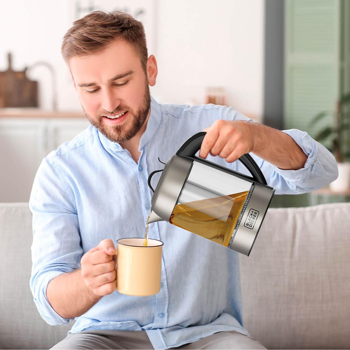 Man fyller vattenkokare med te-filter i ett kök, koppen är gul och vattenkokaren är av glas