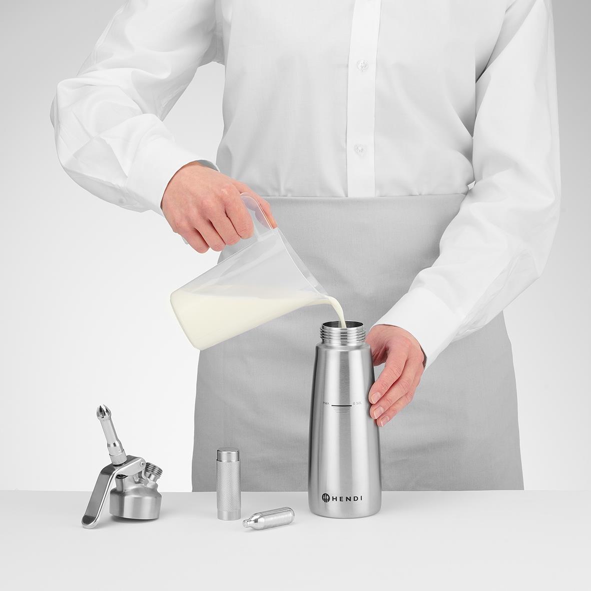 Person häller mjölk från en kanna i en termosflaska på ett vitt bord