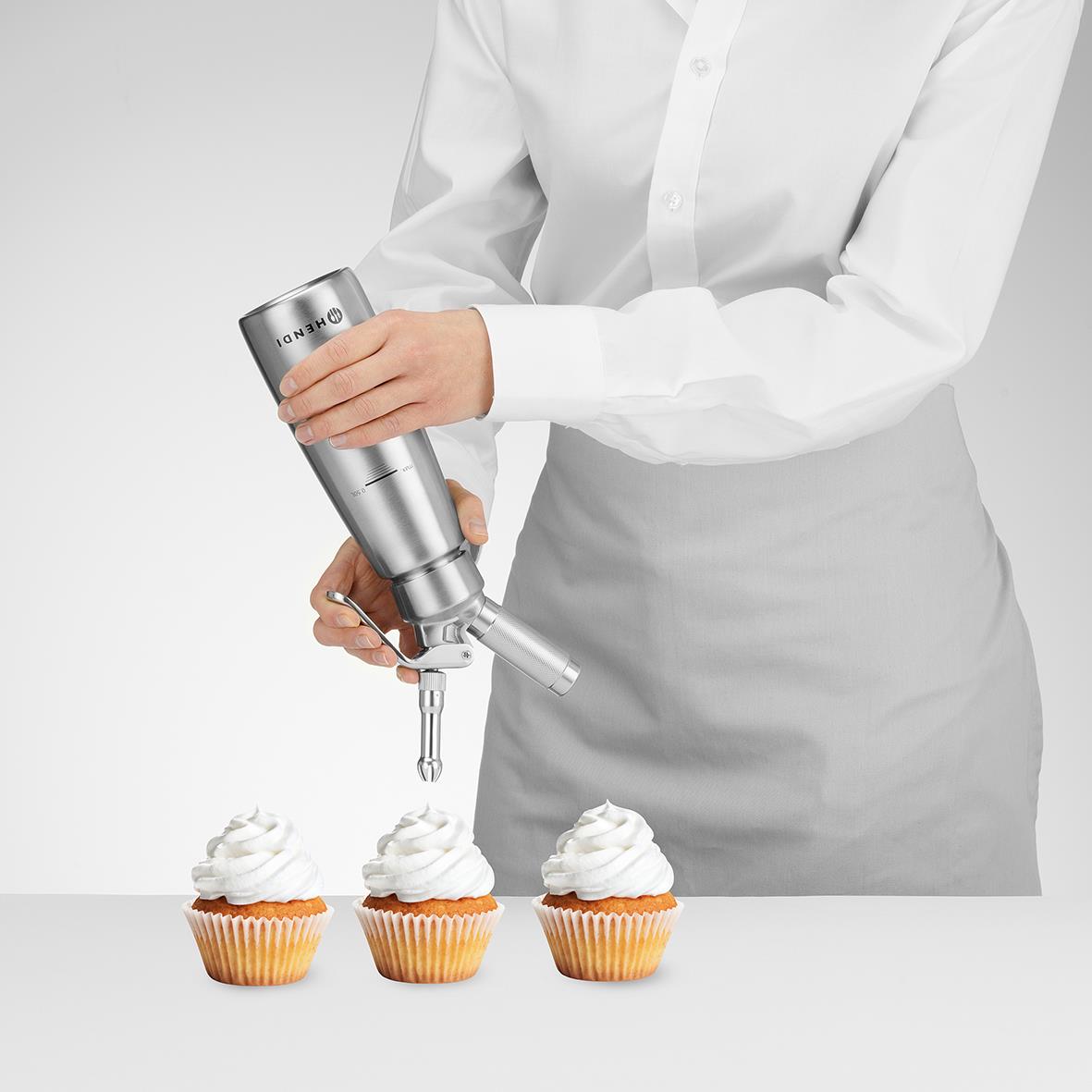 Person sprutar grädde på tre cupcakes med en köksmaskin