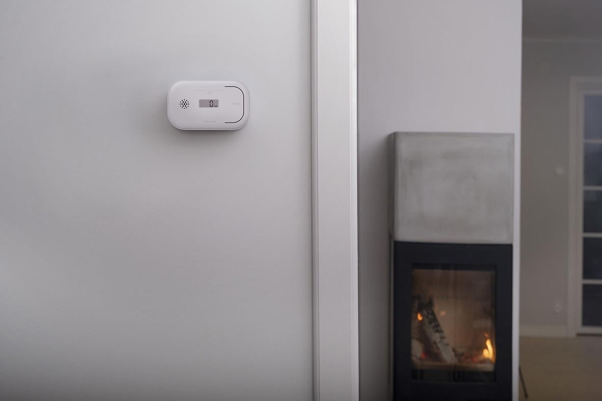 Kolmonoxidlarm Housegard CA108 med LCD-skärm monterad på vägg bredvid en öppen spis