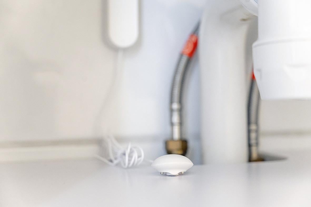 Vattenläckagesensor Housegard placerad nära rör och ledningar på en vägg