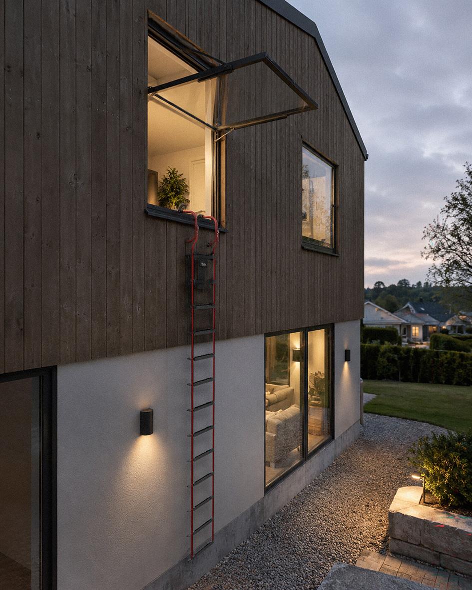 Utomhusbild av ett modernt hus med en brandstege på fasaden, kvällsbelysning och stora fönster