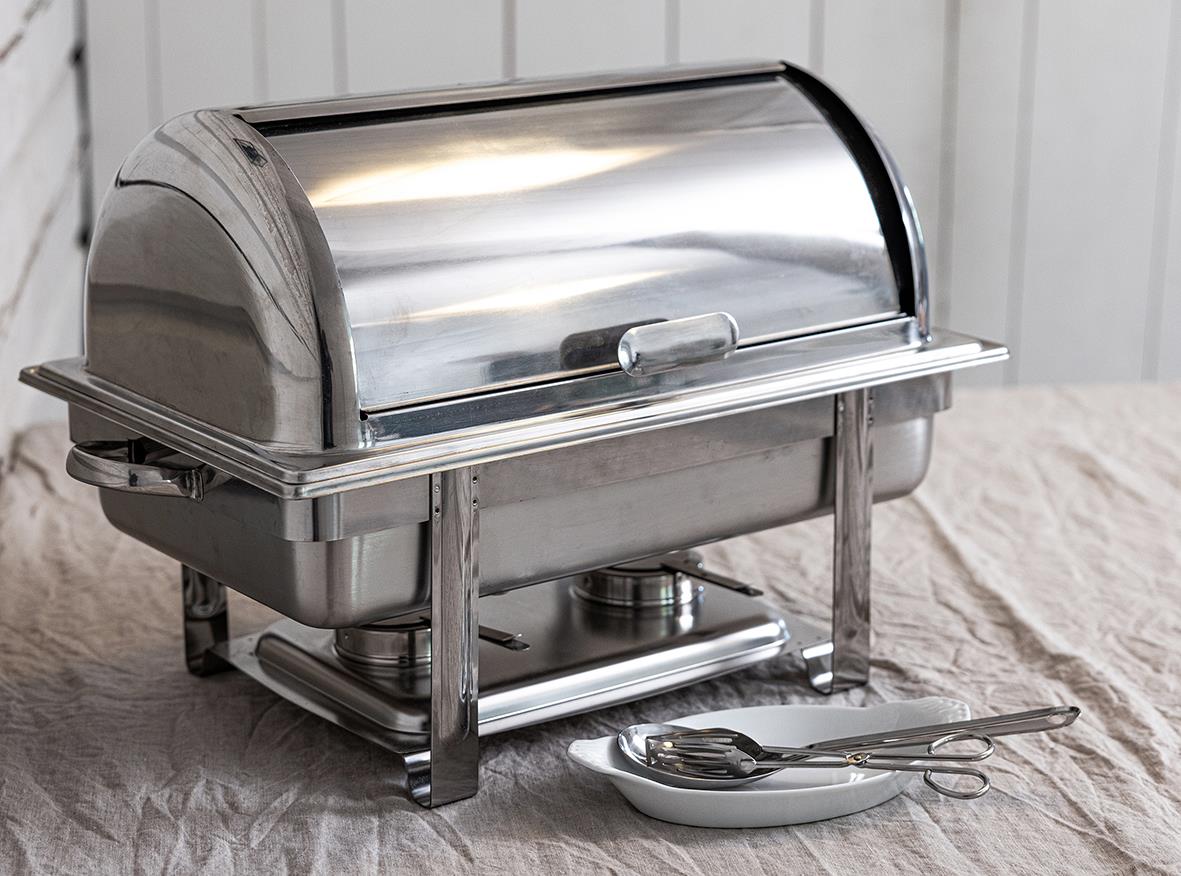 Stålchafing dish på bord med tång och tallrik framför