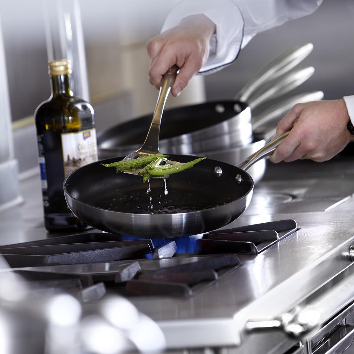 Person steker grön paprika i en svart Scanpan CTX stekpanna på spisen