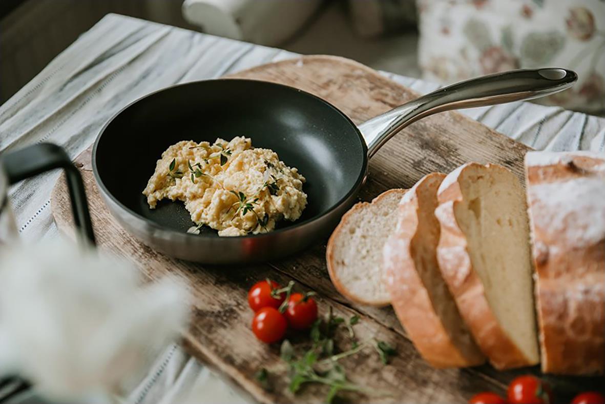 Stekpanna med äggröra, bröd och tomater på träskärbräda