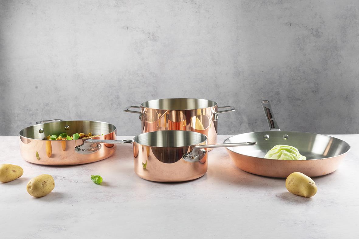 Set med kopparstekpannor Scanpan Maitre D’ Ø28cm på en grå bakgrund med potatis och grönsaker