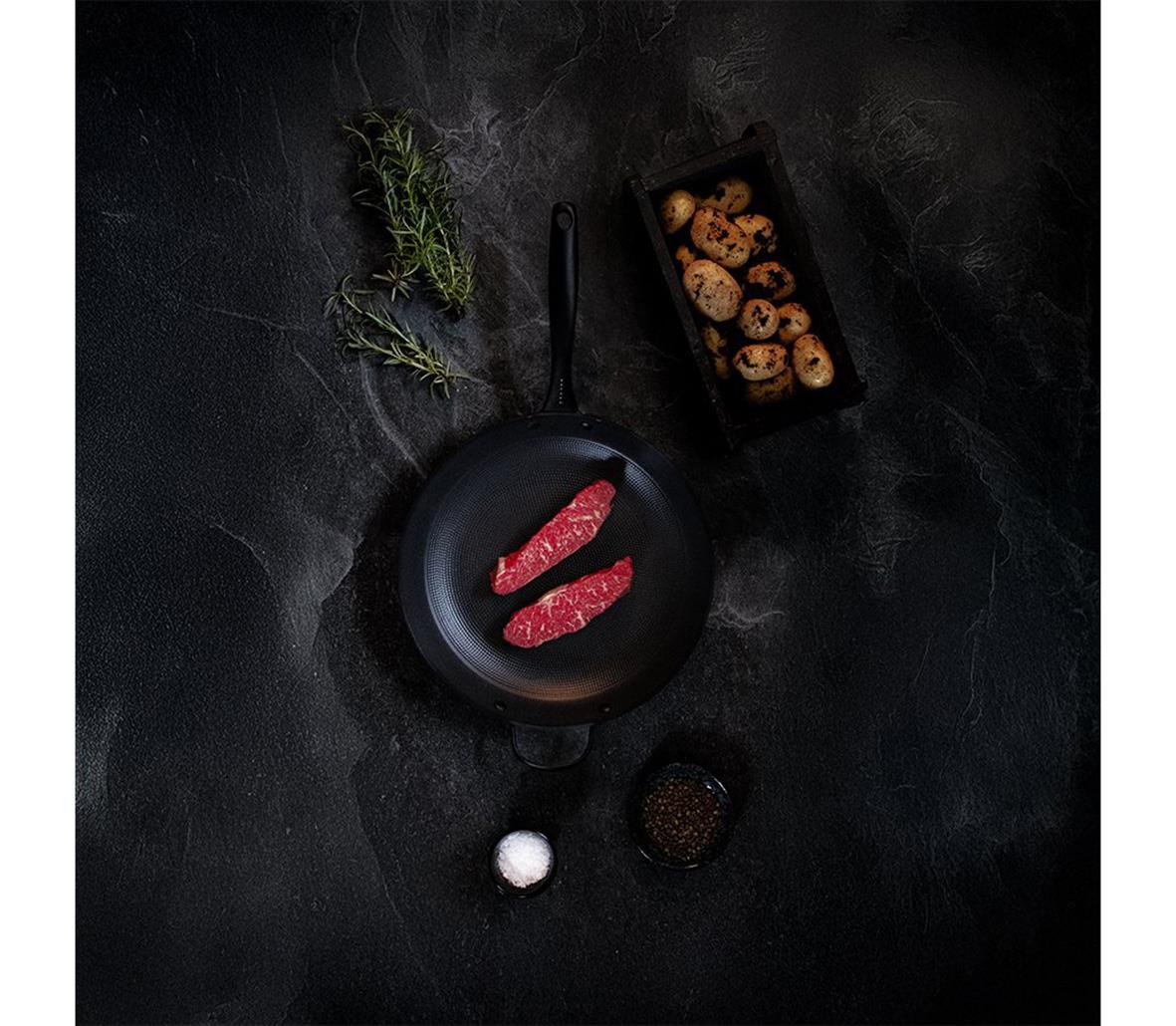 Stekpanna Satake Lättviktsgjutjärn Ø28cm med kött och bakverk på en mörk bakgrund